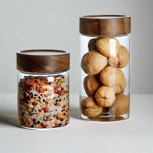 Two glass jars with wooden lids, one containing mixed seeds and the other filled with walnuts, on a white background.